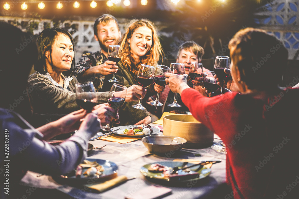Happy family eating and drinking wine at barbecue dinner outdoor - Multiracial mature and young people having fun at bbq sunday meal - Food and summer lifestyle concept - Focus on asian woman face - obrazy, fototapety, plakaty 