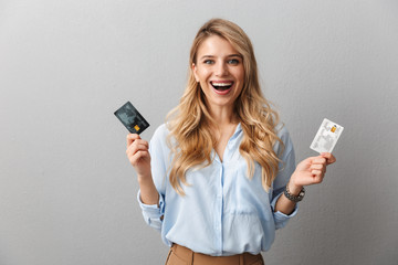 Wall Mural - Pretty blonde business woman posing isolated grey wall background holding two credit cards.