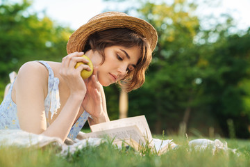 Sticker - Beautiful young pretty woman lies on grass in park outdoors reading book.