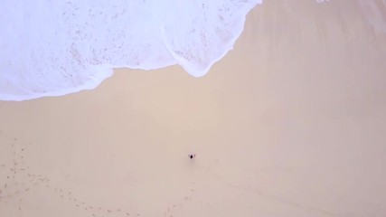 Wall Mural - Aerial drone footage with ocean waves on white sand beach are moving to lonely girl. High top view. Relax bay and clean water.