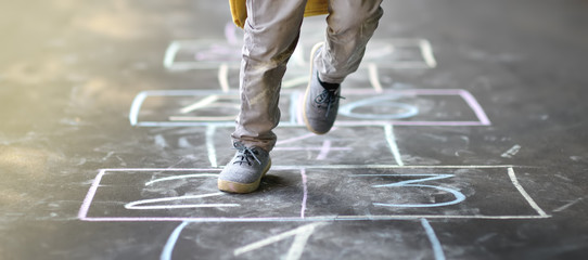 closeup of little boy's legs and hopscotch drawn on asphalt. child playing hopscotch game on playgro