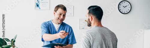 Fotografía panoramic shot of smiling Physiotherapist with diagnosis near patient in hospita
