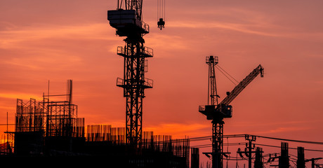 Construction site with crane and sunset sky. Real estate industry. Crane use reel lift up equipment in construction site. Building made of steel and concrete. Crane work against orange sunset sky.