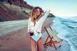 © zamuruev - Pretty blonde woman in the shape of a heart sunglasses, white shirt and stripped swimsuit relaxing on beach and drinks coctail. summer vacation concept.
