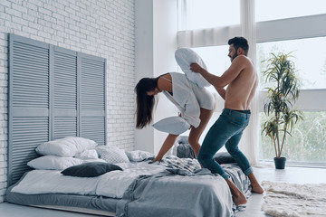 Wall Mural - Lovers and friends. Full length of happy young couple having a fun pillow fight while spending carefree time in the bedroom