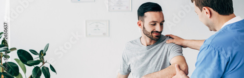 Fotografía panoramic shot of chiropractor massaging arm of patient in hospital with copy sp