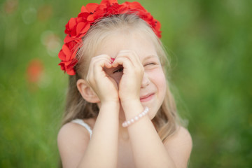 little ukrainian girl looking through heart gesture made with hands in summer green park. Gesture of love to Ukraine by pretty young child in poppy field.