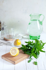 Wall Mural - Preparation of the lemonade drink. Cutted lemon on board with fresh mint. Refreshing, cold, summer drink. Lemonade pitcher. Making traditional, healthy lemonade. Ingredients for making mojito