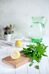 Wall Mural - Preparation of the lemonade drink. Cutted lemon on board with fresh mint. Refreshing, cold, summer drink. Lemonade pitcher. Making traditional, healthy lemonade. Ingredients for making mojito