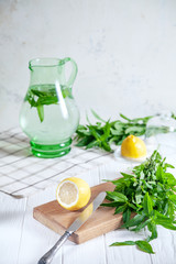 Wall Mural - Preparation of the lemonade drink. Cutted lemon on board with fresh mint. Refreshing, cold, summer drink. Lemonade pitcher. Making traditional, healthy lemonade. Ingredients for making mojito