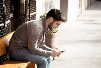 Young attractive happy stylish man on smart phone social network app in european city outdoors