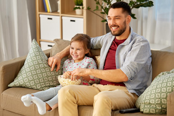 Canvas Print - family, fatherhood and people concept - happy father and daughter with popcorn watching tv at home