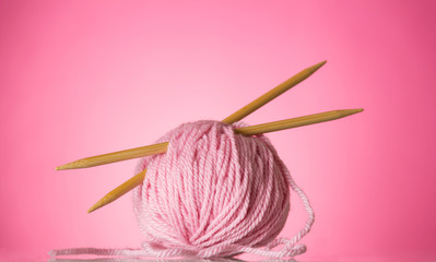 Pink wool ball and knitting needles on bright background