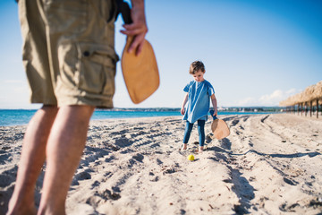 A small girl with unrecognizable father playing outdoors on sand beach.