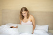 © lashkhidzetim - Smiling young girl relaxing in bed in the morning, using laptop computer.