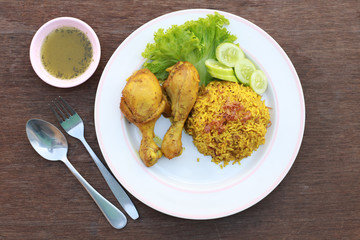 Wall Mural - Muslim yellow rice with chicken in a white plate on a wooden floor