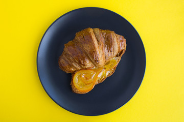 Wall Mural - Croissant with orange marmalade in the dark plate on the yellow background.Top view.