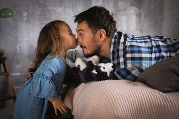 A little girl kisses her dad. Plush doggy in the hands of. Daddy's baby. A man with a beard in a plaid shirt, a daughter in a denim dress. Happy family. Father's day