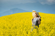 © rodjulian - Smiling pretty girl  in blooming yellow field with mountains on background.