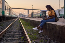 Young Woman Sitting On Platform At The Train Station Using Laptop
