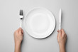 Woman with fork, knife and empty plate on grey background, top view