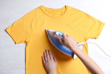 Wall Mural - Woman ironing t-shirt on light background, top view