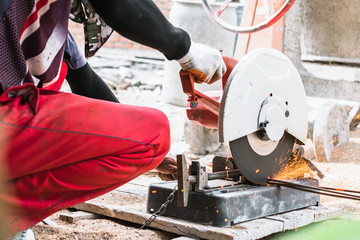 Construction worker cutting steel bar using electric grinder cutting metal.