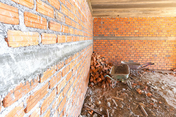 Two wheelbarrow parking inside house under construction with brick wall.