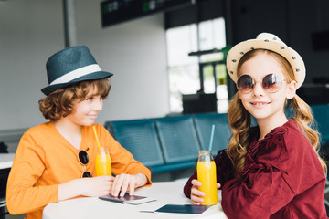 preteen kids sitting at table with orange juice in departure lounge