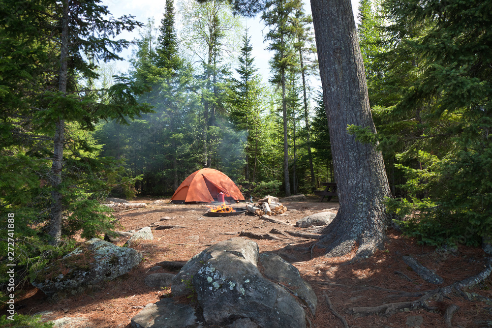 Campsite with orange tent and fire in the northern Minnesota wilderness - obrazy, fototapety, plakaty 