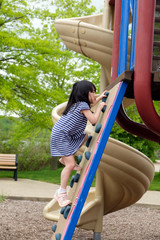 cute asian little girl is climbing up on ladder in playground