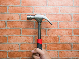 Close-up view of a man's hand holding hammer with brick wall background. Repairing and maintenance. Building and destroying.