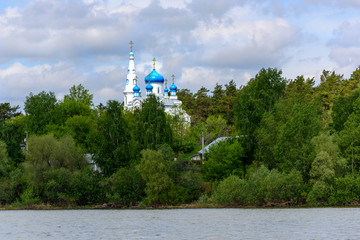 Orthodox Church with blue domes in the forest on the river Bank on a Sunny summer day