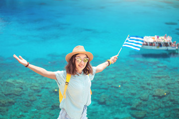 Wall Mural - Happy girl with the Greek flag on the background of the cruise boats in the beautiful Bay of the Mediterranean sea. Travel and water transport in Greece concept