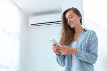 Wall Mural - Young attractive woman control air conditioner temperature using remote controller in room at home.