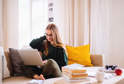 Fotografía A young female student sitting on sofa, using laptop when studying