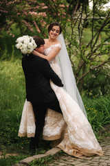 Beautiful wedding couple walking in the park. Bride with long white dress and stylish groom. Pink tree