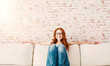 © drubig-photo - junge rothaarige frau sitzt auf der couch zuhause mit brille