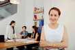 © DragonImages - Portrait of mature confident businesswoman standing with arms crossed and smiling while working with her colleagues during a meeting at office