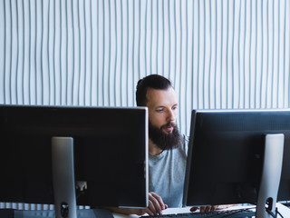 computer programming. bearded software developer using two monitors, working on task at office. copy