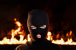 Portrait of young woman in black balaclava against backdrop of a blazing night fire. Concept of mass rallies and riots