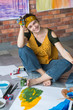 © golubovy - Fine art hobby. Creative young female artist sitting on floor, hands dirty with paint, laughing.