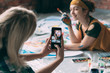 © golubovy - Friends leisure. Lady taking picture of young female artist posing on floor with paint and brush, smiling.
