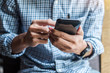 © Jo Panuwat D - Young casual Businessman holding and using smartphone for sms messages, hipster man typing touchscreen cell phone in the cafe. business, lifestyle, technology and Social media network concept