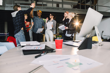 Wall Mural - Young male and female colleagues working with project cooperating each other during meeting in office. Group of casually dressed businesspeople celebrating success