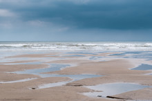 Minimalist Image Of A Flat Sandy Beach At Filey, North Yorkshire, With Numerous Puddles Left Behind By A Low Tide, With Low, Heavy Dark Grey Clouds Reflecting In The Puddles