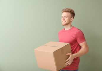 Young man with cardboard box on color background