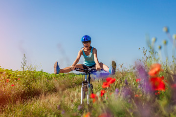 Happy young woman cyclist riding a mountain bicycle in summer field. Girl having fun lifting legs