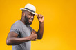 © denis_vermenko - Cheerful carefree young dark-skinned african american man with trendy hat smiling, posing isolated against yellow wall with copy space for your content. Thumbs up.