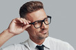 © G-Stock Faces - In his style. Good looking young man adjusting eyewear and smiling while standing against grey background